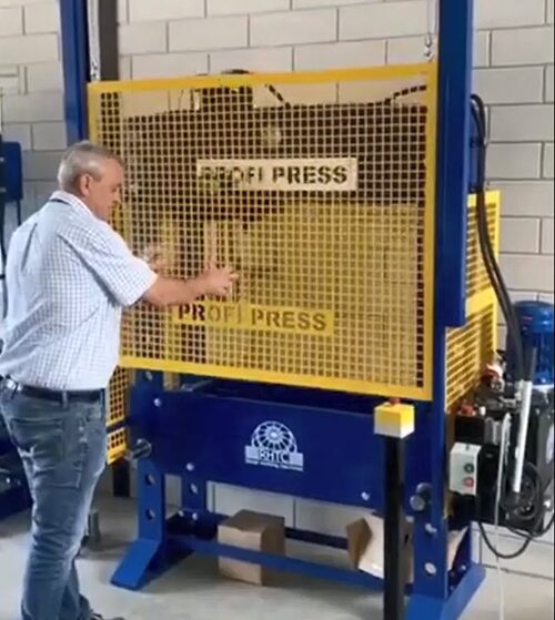 100-ton workshop press with wire mesh front guard, demonstrated by a man.
